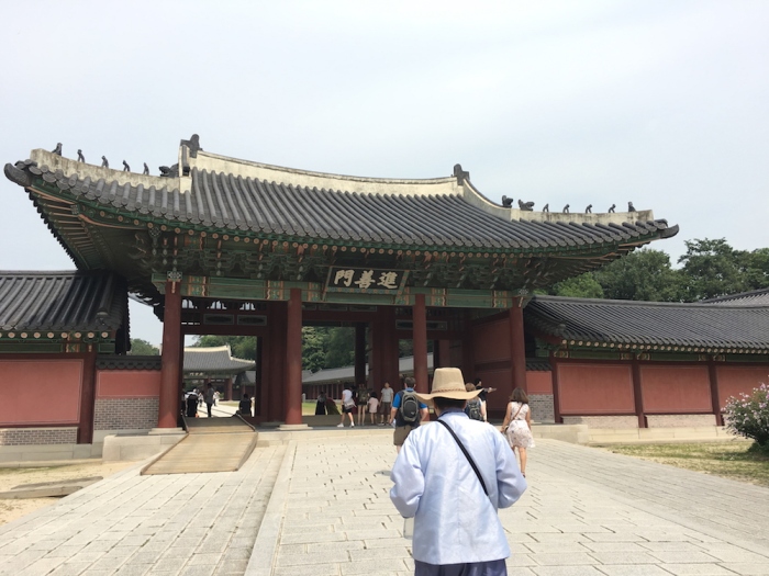 A tour guide in traditional clothes and straw hat leads visitors toward the Main gate of Changdeokgung Palace